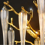 Close up of Clérachic gold branch arms and ribbed clear glass drops with tiny lit bulbs, against a dark studio backdrop.