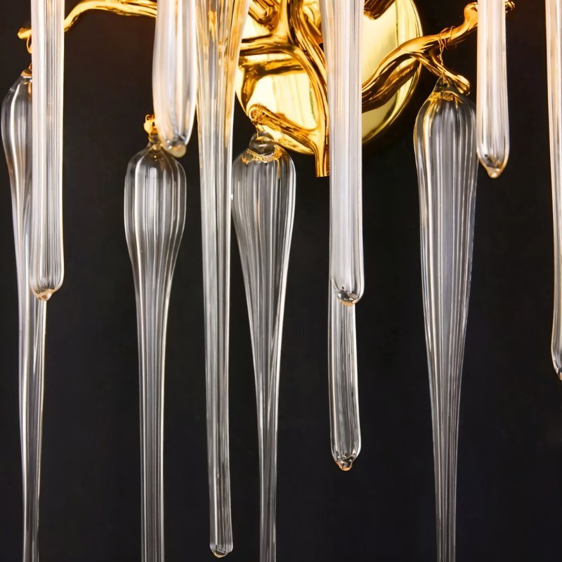 Clérachic wall lamp detail: polished gold backplate, twisting branch arms and long ribbed glass drops on a dark studio ground.