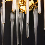 Clérachic wall lamp detail: polished gold backplate, twisting branch arms and long ribbed glass drops on a dark studio ground.