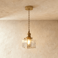 Clérachic gold cube pendant light hangs on a twisted cord, its textured glass shade glowing warm indoors.