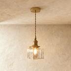 Clérachic gold cube pendant light hangs on a twisted cord, its textured glass shade glowing warm indoors.