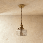 Clérachic gold cube pendant light shown unlit, faceted glass shade hanging against a warm plaster wall.