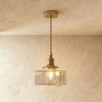 Clérachic gold cube pendant light glows warm, its dimpled glass shade catching light against a plaster wall.