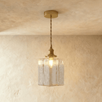 Clérachic gold cube pendant light hangs low from a twisted cord, textured glass shade lit on a plaster wall.