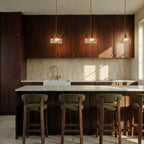 Clérachic gold cube pendant lights hang in a row above a marble kitchen island with dark wood cabinetry.