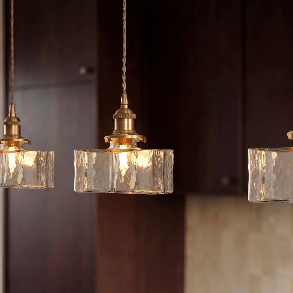 Clérachic gold cube pendant lights glow warm against dark wood kitchen cabinets, textured glass shades close up.