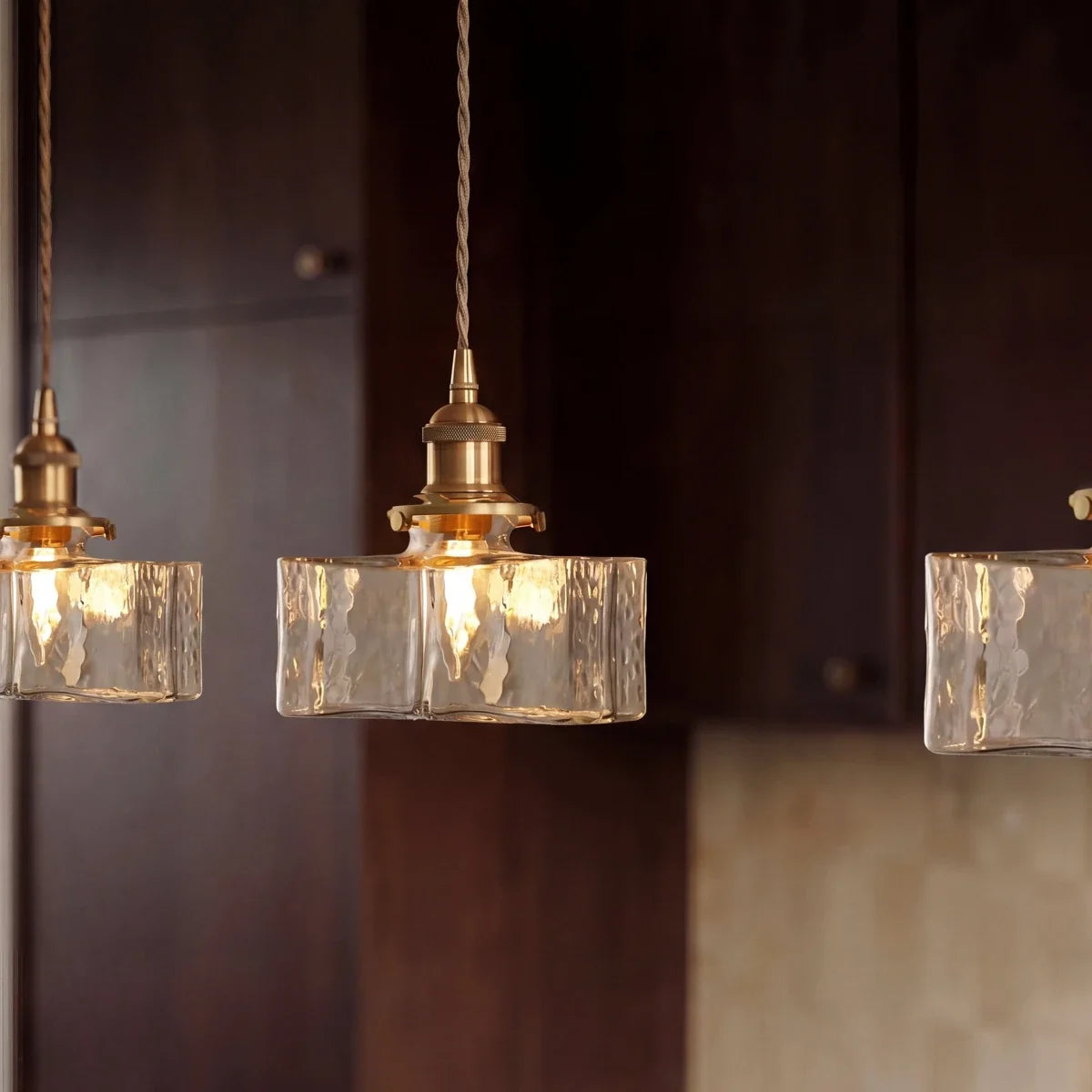 Clérachic gold cube pendant lights glow warm against dark wood kitchen cabinets, textured glass shades close up.