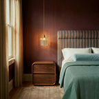 Clérachic gold cube pendant light glows beside a walnut nightstand and striped headboard in a burgundy bedroom.