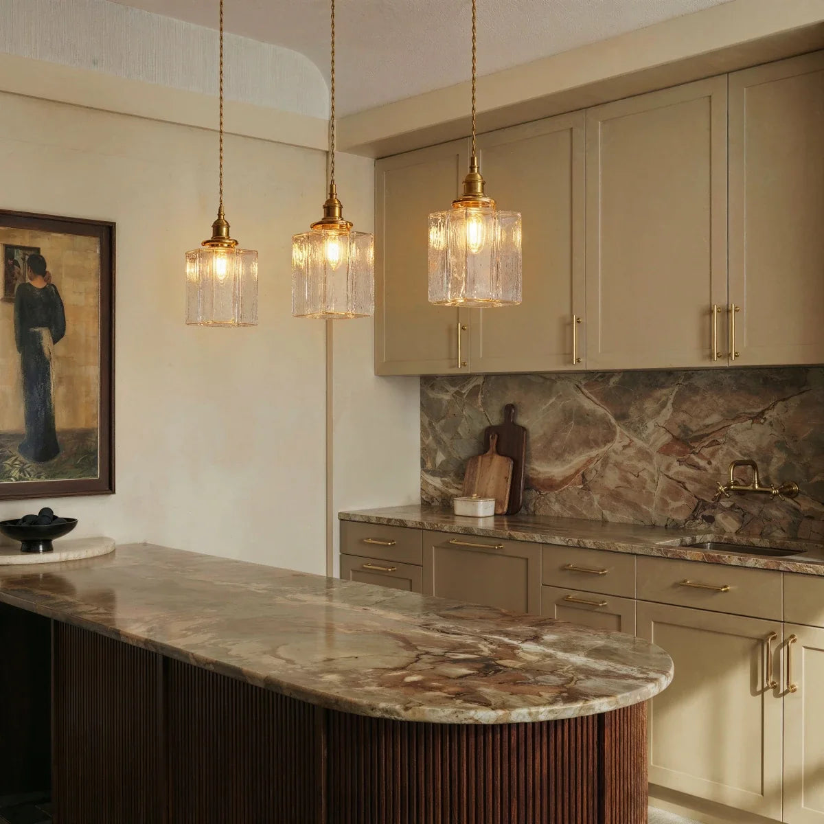 Clérachic gold cube pendant lights hang above a marble kitchen island with cream cabinets and framed art.