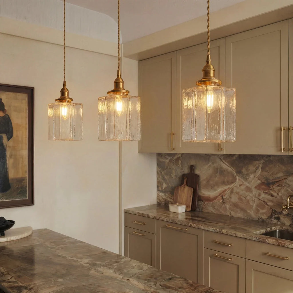 Clérachic gold cube pendant lights cluster above a kitchen counter, cream cabinetry and marble backsplash behind.