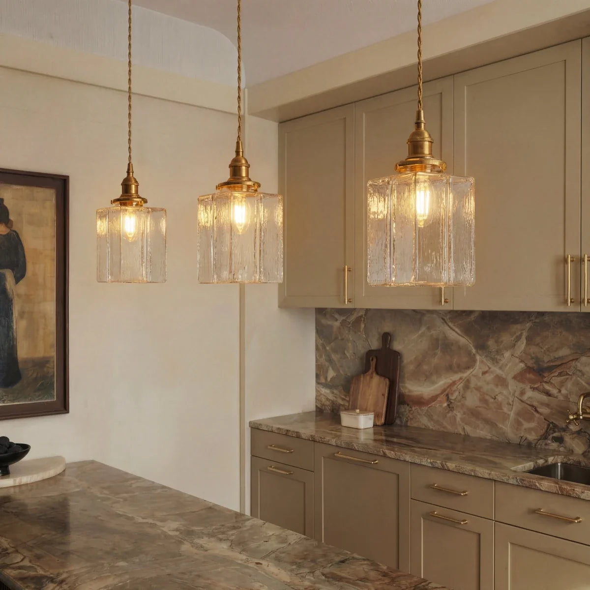 Clérachic gold cube pendant lights cluster above a kitchen counter, cream cabinetry and marble backsplash behind.