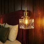 Clérachic close-up of the gold cube pendant's textured glass shade glowing beside a burgundy velvet headboard.