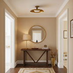 A Clérachic gold dish ceiling light above a narrow entry with a round mirror, a wooden console and a table lamp.