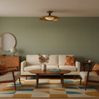 A Clérachic gold ceiling light in a living room with a sage wall, a cream sofa and a geometric rug.