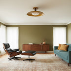 A Clérachic gold ceiling light in an olive-walled living room with a leather lounge chair and a teal sofa.