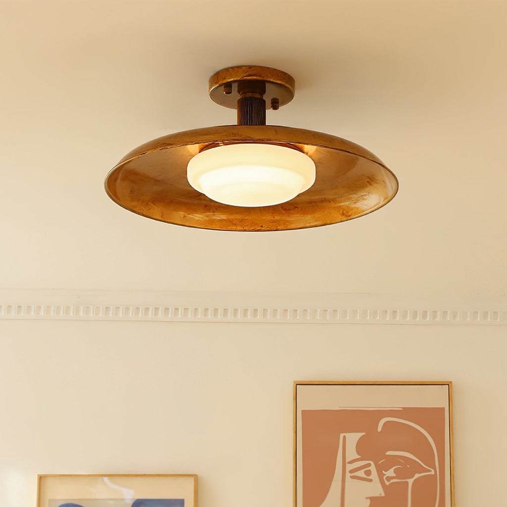 Close view from below of this Clérachic gold ceiling light, its white glass diffuser lit warm inside a mottled gold dish.