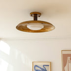 A Clérachic gold dish ceiling light close to a cream ceiling, with framed prints on the wall below.