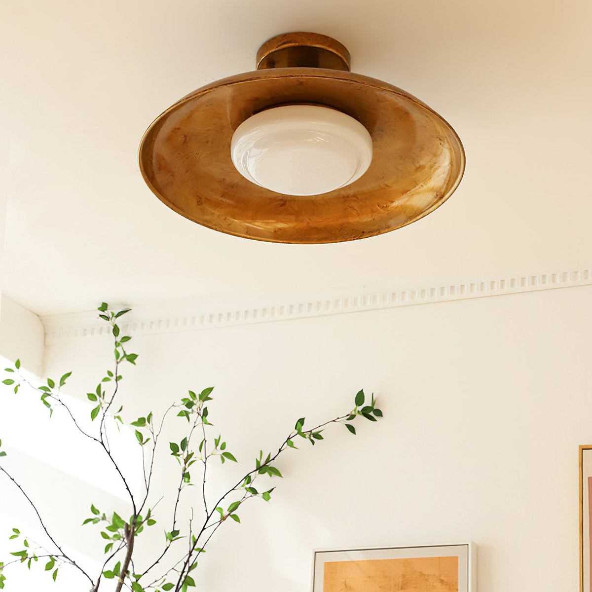 Clérachic gold ceiling light with a green branch in the corner of the frame and a framed print below.