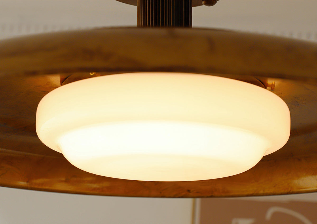 Close view of the lit white glass diffuser in this Clérachic ceiling light, sitting inside the gold dish.