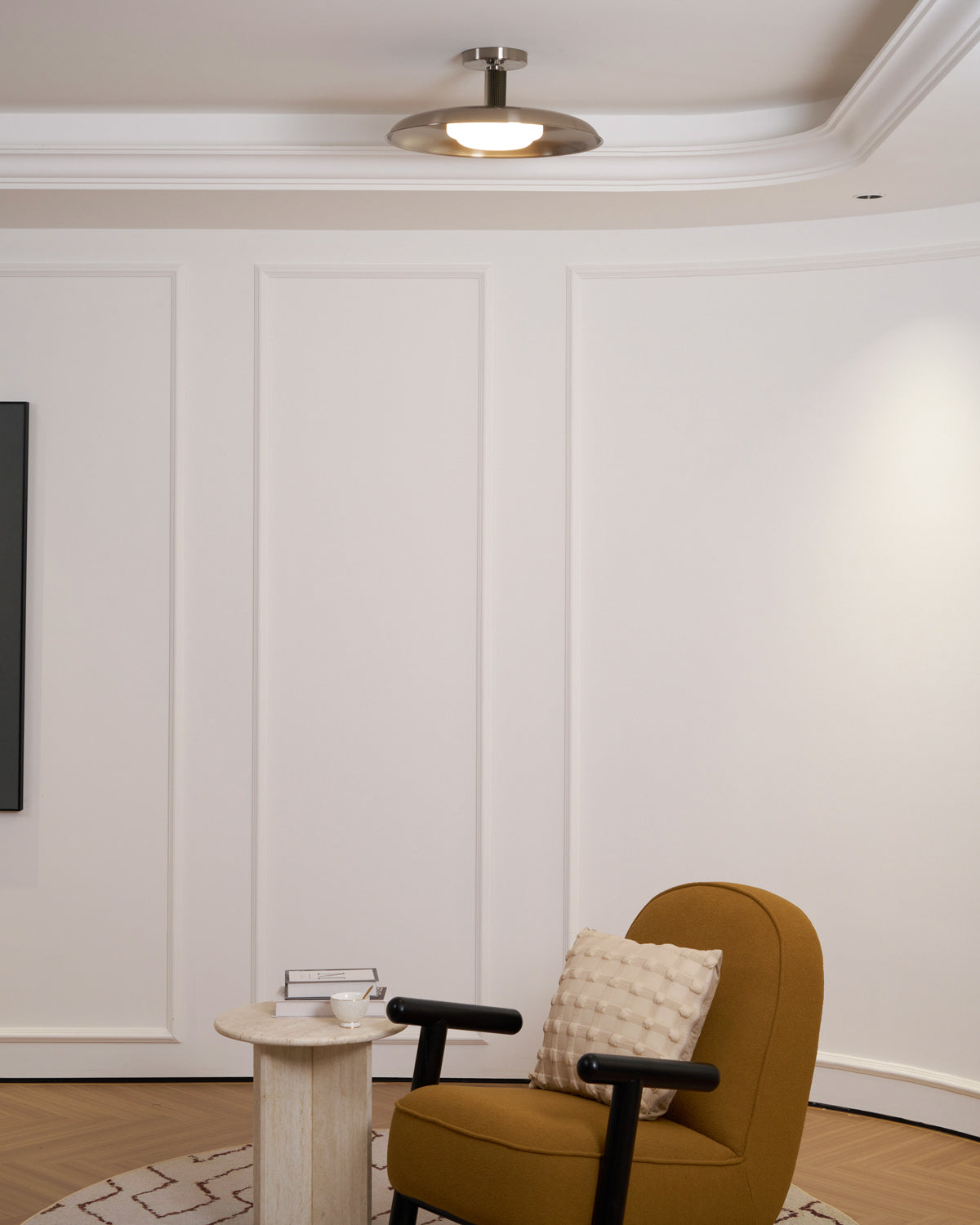 A Clérachic nickel dish ceiling light in a white panelled room with a coved ceiling, above a mustard armchair.
