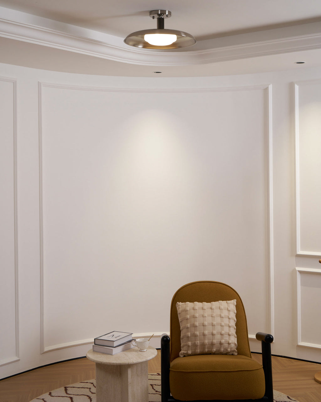 Clérachic nickel ceiling light seen from across a curved white panelled room, with a mustard chair and side table below.