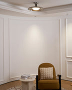 Clérachic nickel ceiling light seen from across a curved white panelled room, with a mustard chair and side table below.