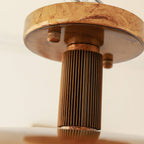 Detail of the round gold canopy and ribbed bronze stem on this Clérachic ceiling light, with a woodgrain-toned finish.