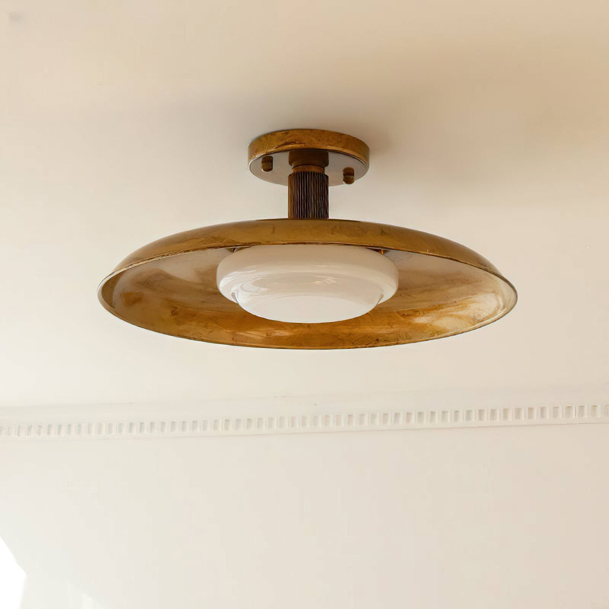 A Clérachic gold ceiling light seen from below, with its white diffuser unlit and a plaster cornice behind.