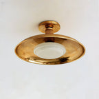 Clérachic gold dish ceiling light seen slightly from the side, with a round canopy and a white glass diffuser below.