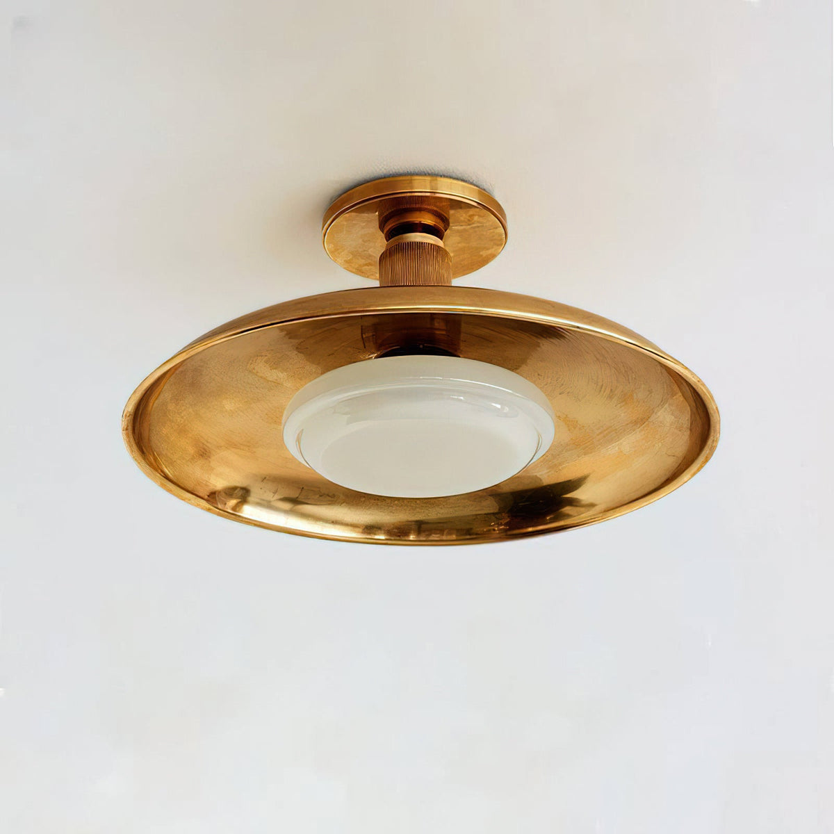 Clérachic gold dish ceiling light seen slightly from the side, with a round canopy and a white glass diffuser below.