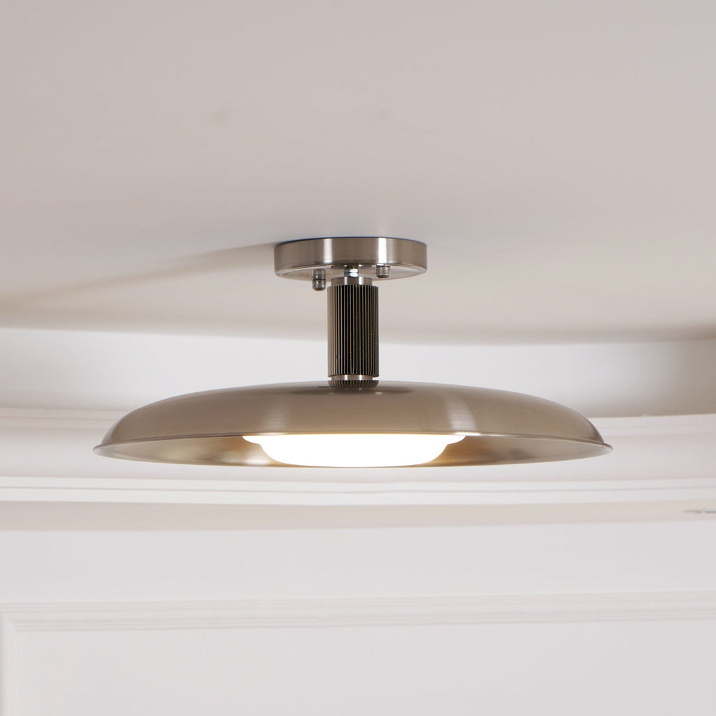 Clérachic nickel dish ceiling light with its diffuser glowing along the lower edge, seen against a white ceiling.