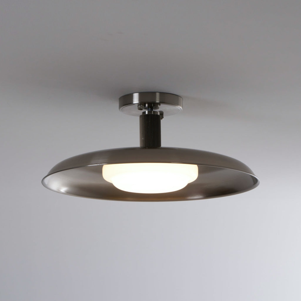 A Clérachic nickel dish ceiling light with its white diffuser lit, against a soft grey ceiling.