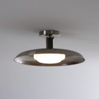 A Clérachic nickel dish ceiling light with its white diffuser lit, against a soft grey ceiling.