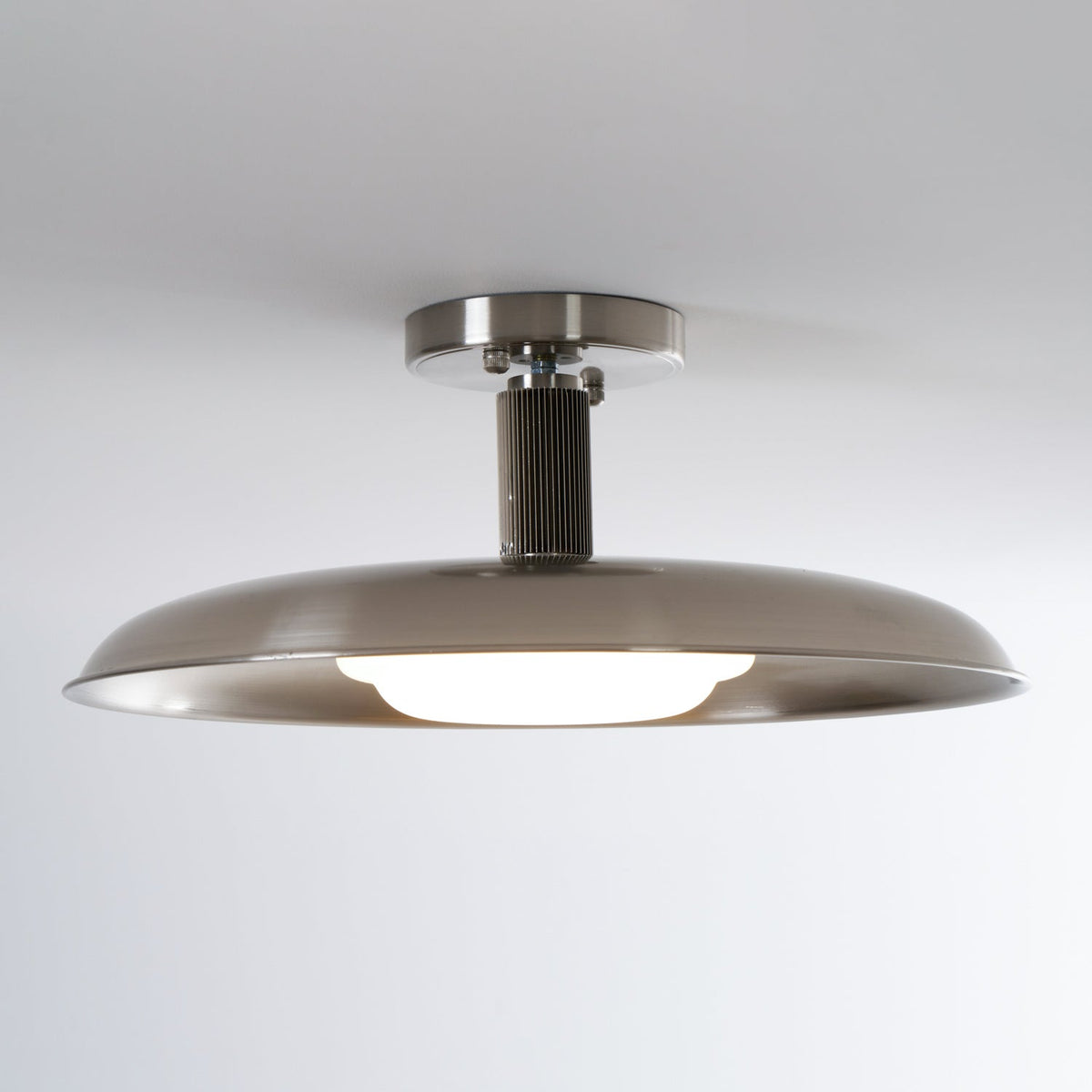 Wider view of this Clérachic nickel ceiling light, lit warm, with a ribbed dark stem and a broad shallow dish.