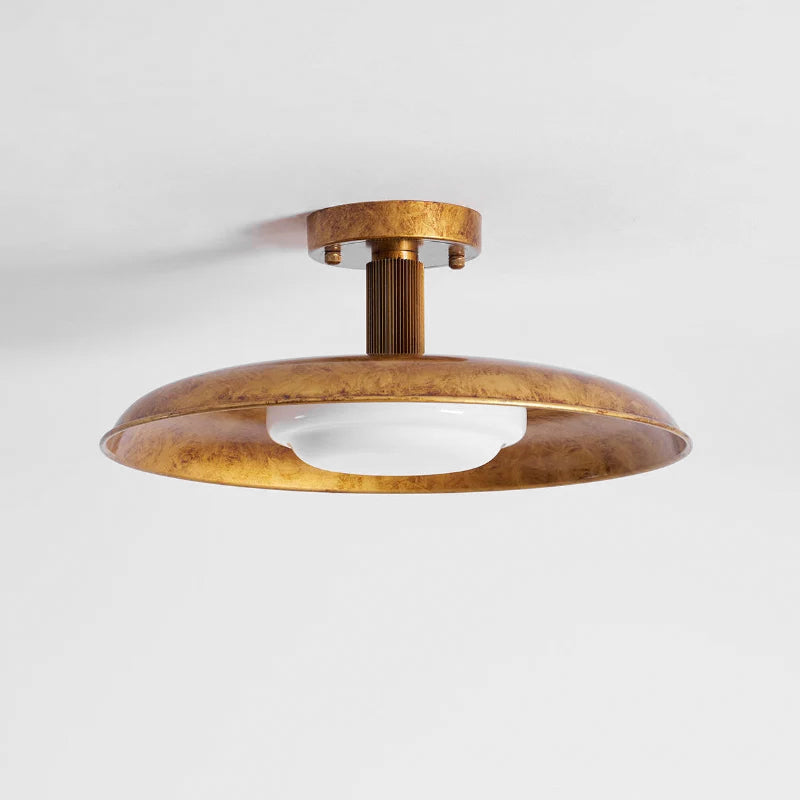 Gold Clérachic dish ceiling light with a mottled brass finish and a white diffuser, against a pale ceiling.