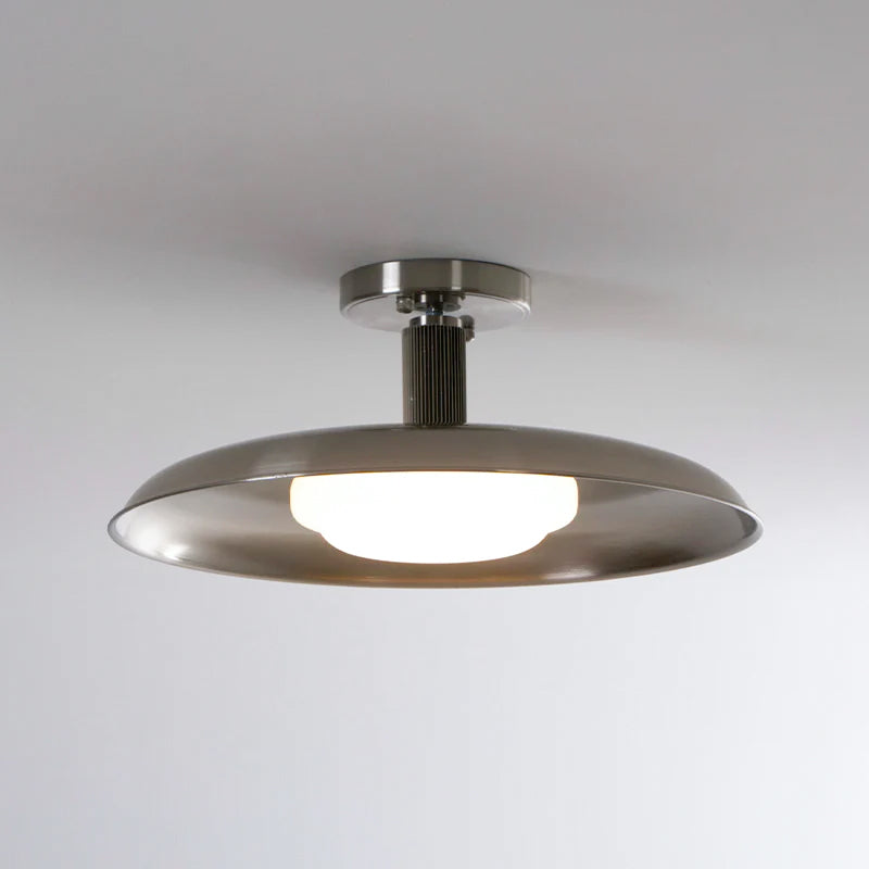 A Clérachic nickel dish ceiling light, lit, with a round nickel canopy and ribbed stem against a soft grey ceiling.