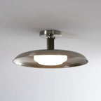 A Clérachic nickel dish ceiling light, lit, with a round nickel canopy and ribbed stem against a soft grey ceiling.