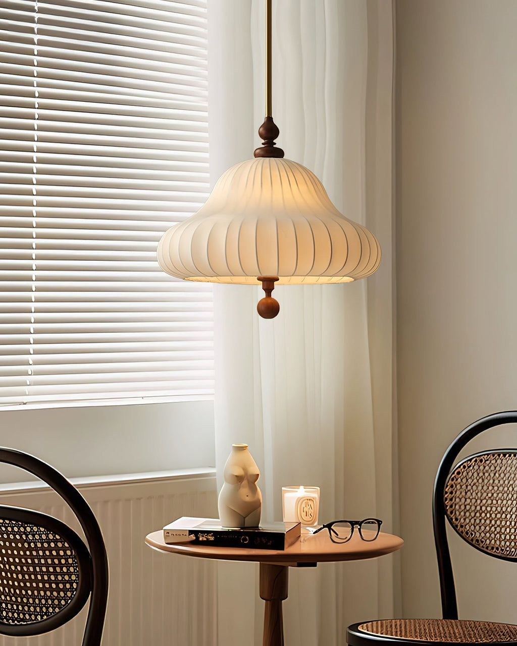 Beside a window with white blinds and a sheer curtain, this Clérachic pendant hangs above a small round table with a candle and glasses.