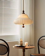 Beside a window with white blinds and a sheer curtain, this Clérachic pendant hangs above a small round table with a candle and glasses.