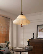 This Clérachic pendant glows in a panelled room above a dark round table stacked with books, with a wooden cabinet behind.
