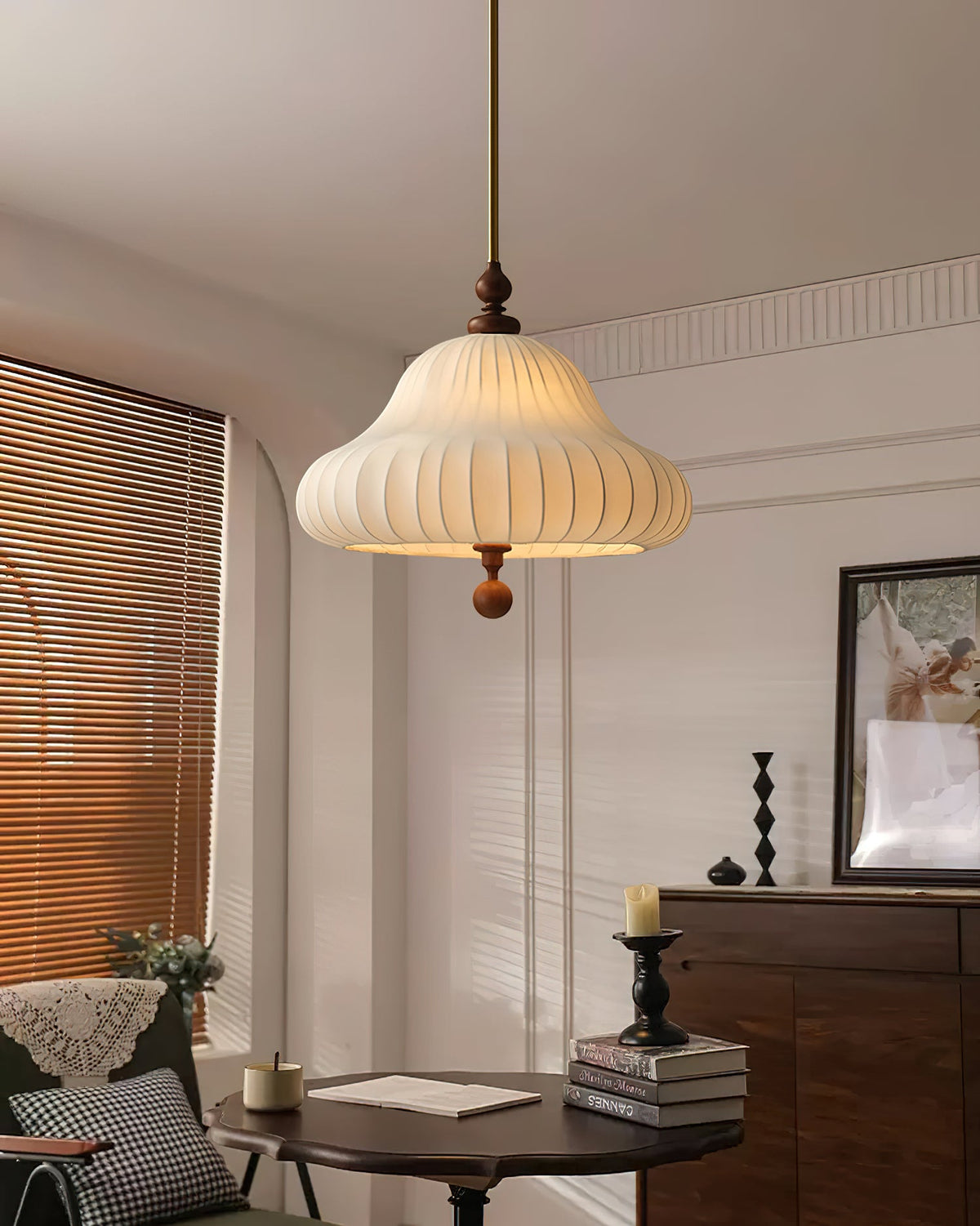 This Clérachic pendant glows in a panelled room above a dark round table stacked with books, with a wooden cabinet behind.