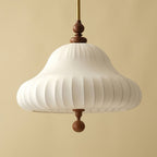 Close view from below of the ribbed white fabric shade, walnut neck and walnut ball drop on this Clérachic pendant, against a sand-coloured wall.