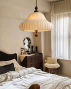 Above a bed with white bedding and a dark headboard, this Clérachic pendant is lit near a dresser and a sheer-curtained window.
