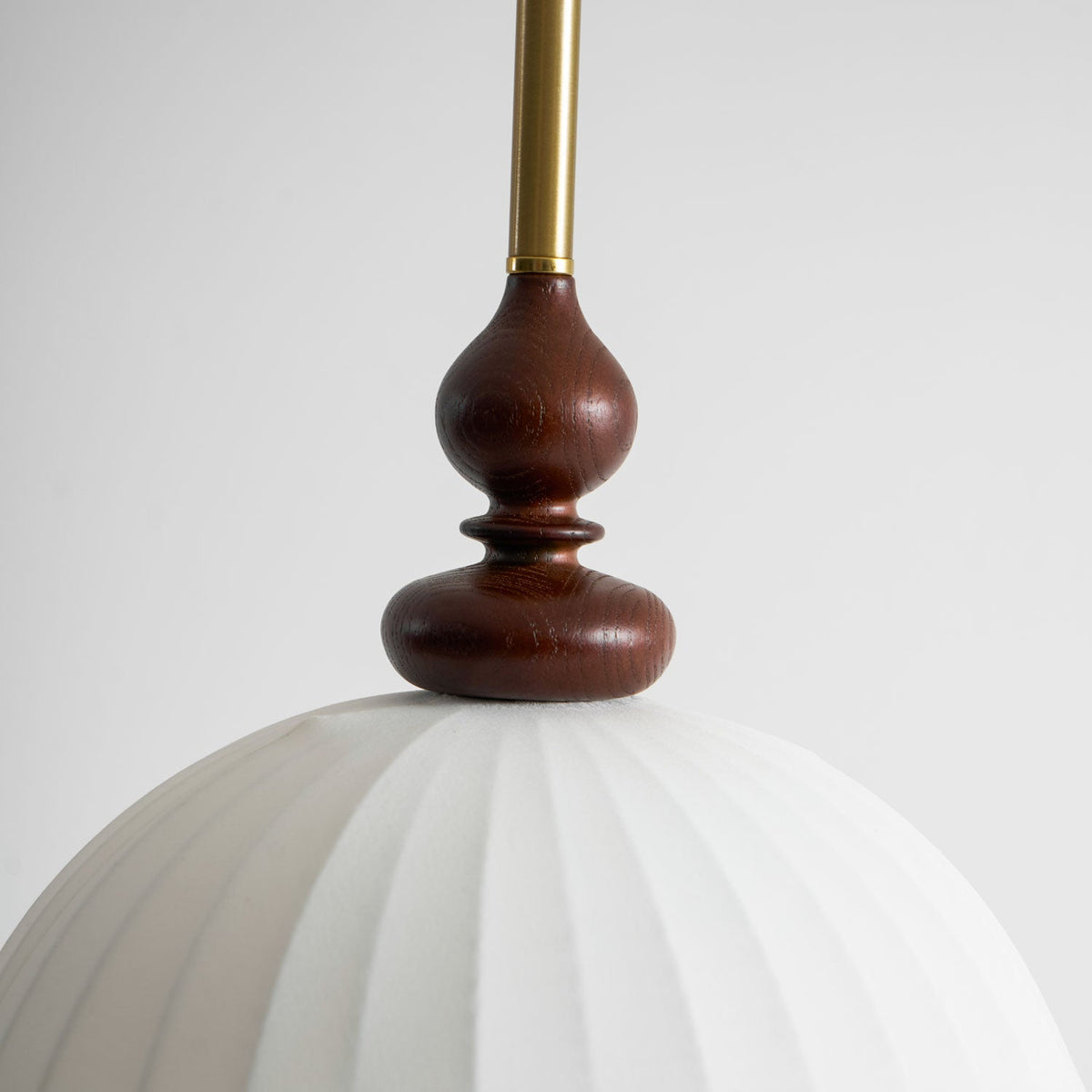Close view of the turned walnut finial and brass rod where they meet the white pleated shade of this Clérachic pendant.