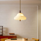 Lit pendant with a ribbed white shade from Clérachic, hanging in front of a panelled wall above a round table with a green book.