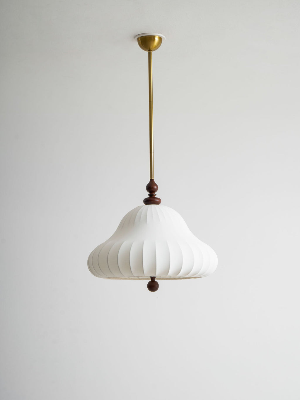 Unlit white ribbed shade of this Clérachic pendant hanging from a brass rod and canopy against a pale grey wall.