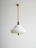 Unlit white ribbed shade of this Clérachic pendant hanging from a brass rod and canopy against a pale grey wall.