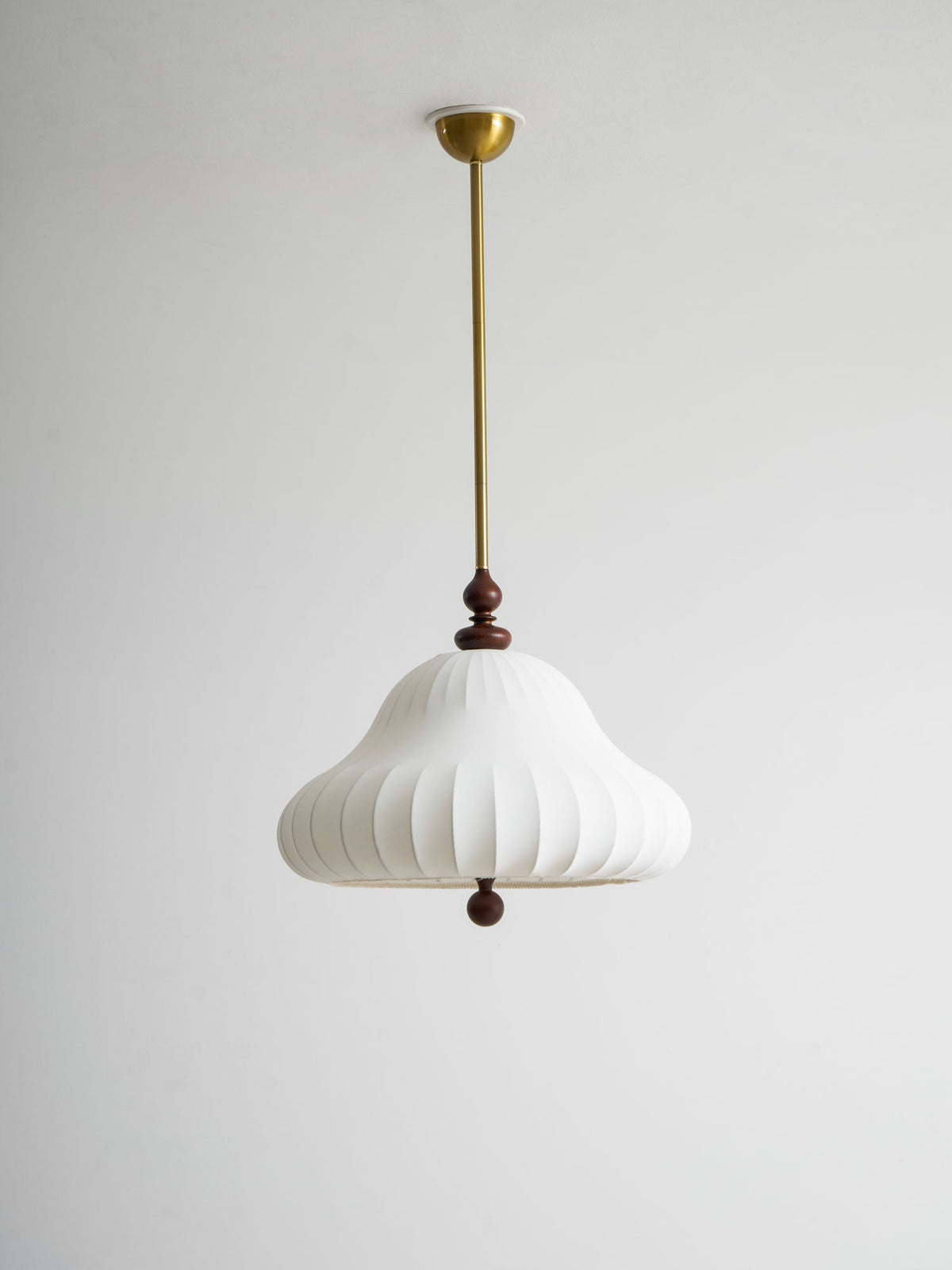 Unlit white ribbed shade of this Clérachic pendant hanging from a brass rod and canopy against a pale grey wall.