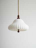 Low, close view of the white pleated bell shade of this Clérachic pendant, with the walnut neck above and ball below, on grey.