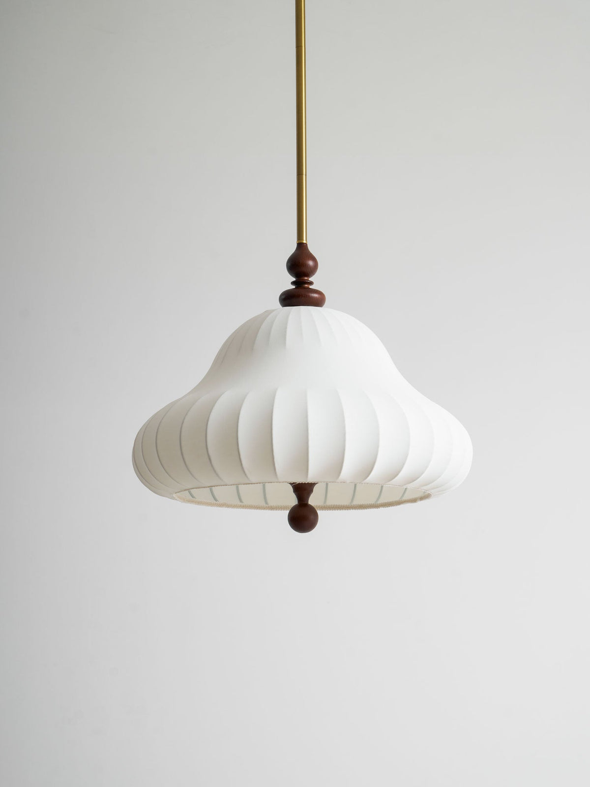 Low, close view of the white pleated bell shade of this Clérachic pendant, with the walnut neck above and ball below, on grey.
